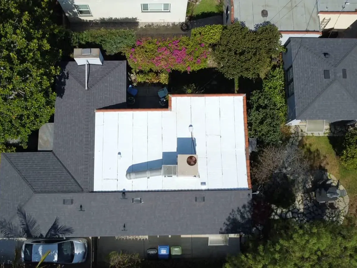 Aerial view of a light-colored low-slope roof beside dark shingle roof sections