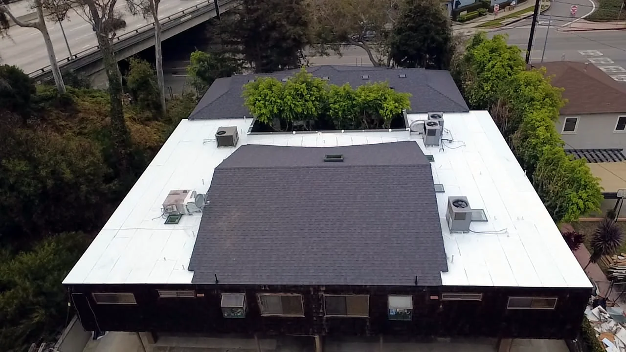 Aerial view of a mixed roof system — dark shingles over a white reflective flat roof — near Barrington in West Los Angeles