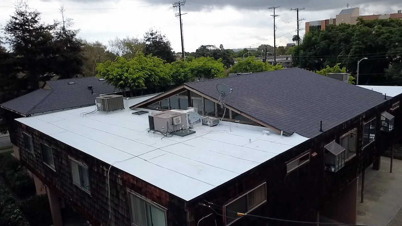 Clerestory gable and dark shingle roof meeting a white flat roof on a West LA apartment building